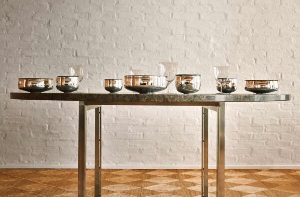PUIFORCAT-MOOD-Collection-Selene-1-1200w-100KB A lifestyle photo of the Puiforcat Selene Collection featuring a gathering of several sterling silver vases and bowls on a dining table.