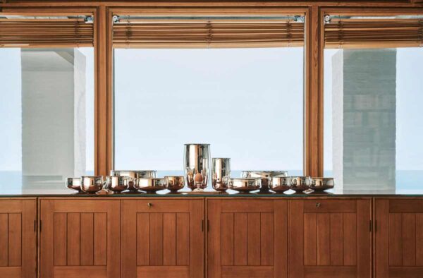 PUIFORCAT-MOOD-Collection-Selene-2-1200w-100KB A lifestyle photo of the Puiforcat Selene Collection featuring a gathering of several sterling silver vases and bowls on a credenza in front of a window.