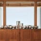 A lifestyle photo of the Puiforcat Selene Collection featuring a gathering of several sterling silver vases and bowls on a credenza in front of a window.