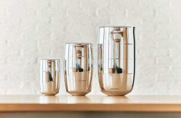 PUIFORCAT-MOOD-Collection-Selene-5-1200w-100KB A lifestyle photo of the Puiforcat Selene Collection featuring the 3 sizes of sterling silver vases on a shelf.