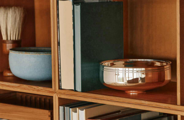 PUIFORCAT-MOOD-Collection-Selene-6-1200w-100KB A lifestyle photo of the Puiforcat Selene Collection including sterling silver bowls and vases. A large Selene bowl is pictured on a book shelf.