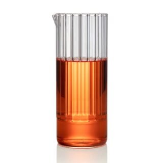 Minimalist studio setting with an amber-toned beverage in a Fferrone Flight Carafe made of borosilicate glass featuring a tall fluted cylindrical design | Kneen & Co