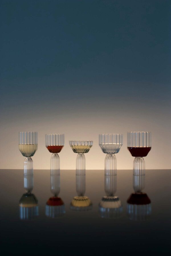 Sophisticated lounge setting with Fferrone Margot Glassware in fluted borosilicate glass featuring an assortment of wine and champagne glasses with colorful liquids and reflections | Kneen & Co