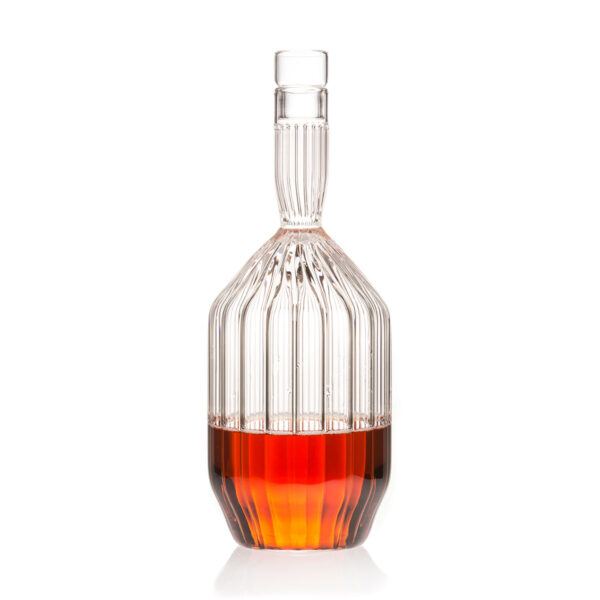 Minimalist studio setting with an amber spirit in a Fferrone Margot Decanter made of borosilicate glass featuring a tall neck and intricate fluted body | Kneen & Co