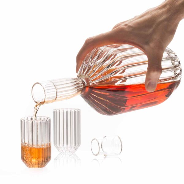 Lifestyle studio setting with a hand pouring spirits from a Fferrone Margot Decanter into Margot Mini Glasses in borosilicate glass highlighting the collection's textural fluting | Kneen & Co