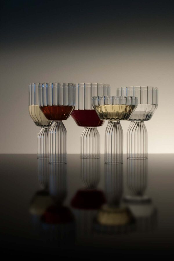Sophisticated lounge setting with Fferrone Margot Glassware in fluted borosilicate glass featuring an assortment of wine and champagne glasses with colorful liquids and reflections | Kneen & Co