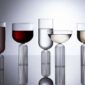 Elegant studio setting with Fferrone May Glassware in fluted borosilicate glass featuring an assortment of wine, water, and champagne glasses filled with various spirits and reflecting on a dark surface | Kneen & Co