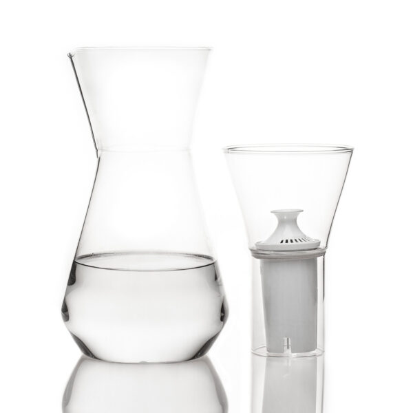 Minimalist studio display of a Fferrone Talise Carafe in clear borosilicate glass featuring a smooth tapered carafe partially filled with water alongside a matching funnel with a white filter insert | Kneen & Co