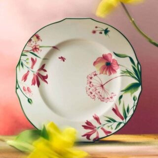 GINORI-FLORENZA-SET-03-0084-1200w-100KB A soft, pink-lit setting with a Ginori 1735 Florenza collection dinner plate, featuring fine porcelain with a floral motif and scalloped edge, framed by blurred yellow flowers | Kneen & Co