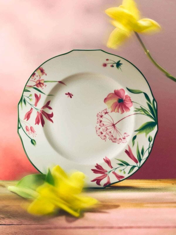 A soft, pink-lit setting with a Ginori 1735 Florenza collection dinner plate, featuring fine porcelain with a floral motif and scalloped edge, framed by blurred yellow flowers | Kneen & Co