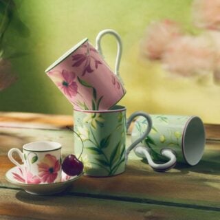Sun-dappled outdoor wooden table with Ginori 1735 Florenza mugs and coffee cup in fine porcelain featuring pink and green floral patterns with a single cherry | Kneen & Co