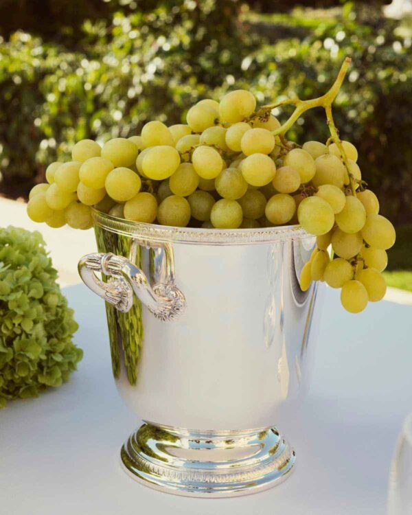 Sunlit outdoor garden setting featuring a Christofle Malmaison Champagne Bucket in silver plate with signature Empire-style leaf borders and ornate handles | Kneen & Co