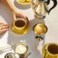 Sun-drenched tea service featuring the Christofle Malmaison Riviera Tea Cup and Saucer in yellow Limoges porcelain paired with silver-plated holloware | Kneen & Co
