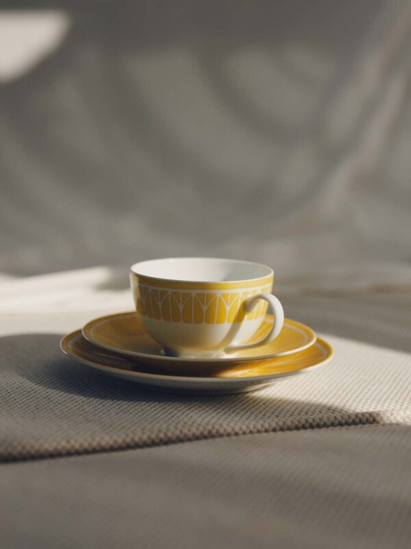 CHRISTOFLE-MALMAISON-RIVIERA-2026-RGB-HD-21-1200w-100KB Lifestyle shot of a Christofle Malmaison Riviera Tea Cup and Saucer in yellow Limoges porcelain | Kneen & Co