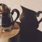 Artistic lifestyle setting featuring a Christofle Malmaison Silver-Plated Water Pitcher finished with a contrasting matte black ebony handle and intricate Empire-style leaf engravings on the base | Kneen & Co