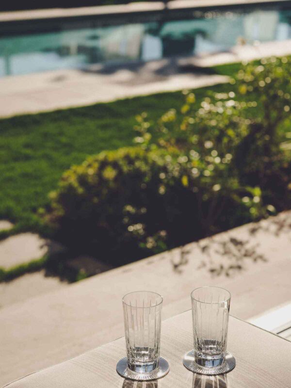 Sunlit casual lifestyle setting featuring Christofle Malmaison crystal tumblers showcasing deep vertical light-refracting cuts | Kneen & Co