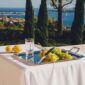 Sunlit outdoor Mediterranean setting featuring a handled silver-plated serving tray from the Christofle Malmaison collection and a crystal water tumbler | Kneen & Co