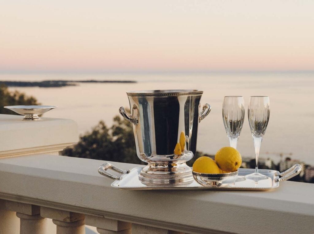 Serene coastal sunset setting featuring a Christofle Malmaison Champagne Bucket and silver-plated handled tray with crystal stemware | Kneen & Co