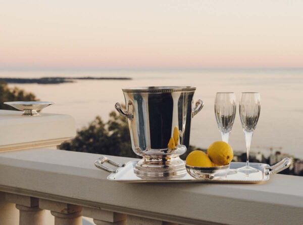 Serene coastal sunset setting featuring a Christofle Malmaison Champagne Bucket and silver-plated handled tray with crystal stemware | Kneen & Co