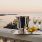 Serene coastal sunset setting featuring a Christofle Malmaison Champagne Bucket and silver-plated handled tray with crystal stemware | Kneen & Co
