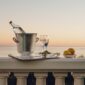 Serene coastal sunset setting featuring a Christofle Malmaison Champagne Bucket and handled tray in mirror-polished silver plate with signature Empire-style leaf borders and crystal flutes | Kneen & Co