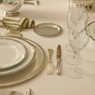 Close-up of a formal place setting featuring Christofle Malmaison porcelain plates and silver-plated flatware | Kneen & Co