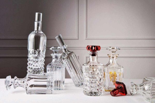 BACCARAT-1702352-1703341-Lifestyle-1200w-100KB (1) Baccarat crystal decanters from the Harcourt 1841, Harmonie, and Louxor collections displayed together on a refined tabletop, showcasing handcrafted French crystal, architectural silhouettes, and signature cut patterns. | Kneen & Co.