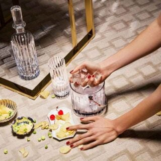 BACCARAT-1703341-1894083-2816795-lifestyle-1200w-100KB Baccarat Harmonie crystal barware, including a whiskey decanter, highball glasses, and ice bucket, arranged for cocktail service with ice and appetizers, showcasing the collection's signature fluting and contemporary French crystal craftsmanship | Kneen & Co