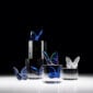 A collection of Baccarat Lucky Butterfly crystal sculptures in blue, iridescent, and clear crystal displayed on sculptural black and clear acrylic pedestals, highlighting Evelyne Julienne's graceful butterfly design and Baccarat's exceptional French crystal craftsmanship | Kneen & Co