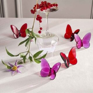 Baccarat Lucky Butterflies crystal sculptures in red and pink displayed with fresh flowers and an inverted crystal wine glass on a tabletop | Kneen & Co