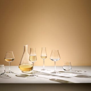 Lifestyle image of the Château Baccarat Stemware collection featuring handcrafted Baccarat crystal wine glasses, champagne flute, tumbler, and decanter arranged on a softly lit table | Kneen & Co