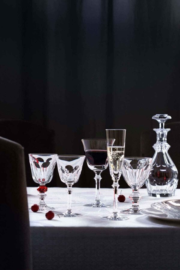 Baccarat Harcourt Eve crystal stemware and decanter displayed on a white linen table, featuring wine glasses, Champagne flutes, and a crystal decanter with the collection's signature hexagonal bases and elegant contemporary silhouettes | Kneen & Co