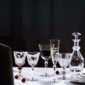 Baccarat Harcourt Eve crystal stemware and decanter displayed on a white linen table, featuring wine glasses, Champagne flutes, and a crystal decanter with the collection's signature hexagonal bases and elegant contemporary silhouettes | Kneen & Co