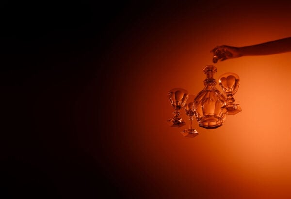 Baccarat Harcourt Eve crystal stemware and decanter suspended against a warm amber background, showcasing the collection's signature hexagonal bases and elegant contemporary silhouettes | Kneen & Co