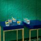 Baccarat Everyday Classic crystal tumblers displayed on deep blue lacquer tables against an emerald green textured wall, each glass featuring a unique cut pattern and garnished cocktails that showcase the collection's versatile design | Kneen & Co