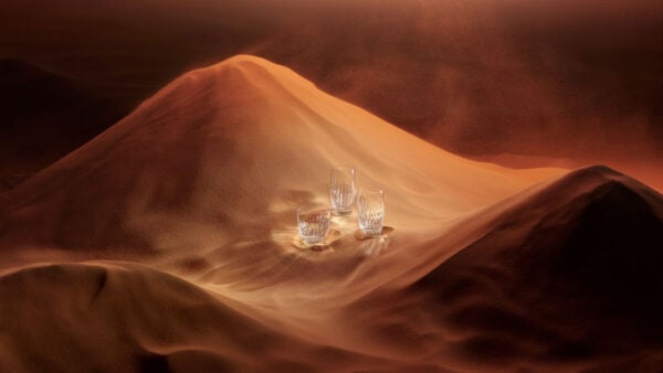 BACCARAT-2811294-Lifestyle-1200w-100KB Baccarat Masséna crystal highball glasses and tumbler displayed on sculpted sand dunes, highlighting the collection's signature deep bevel cuts and brilliant light-reflecting crystal | Kneen & Co