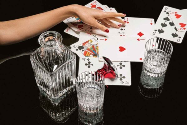 BACCARAT-2811298-1845261-2811293-2811299-2813210-1704365-Lifestyle-1200w-100KB Baccarat Harmonie crystal tumblers and matching whiskey decanter displayed with playing cards, showcasing the collection's signature vertical fluting for refined whisky service and cocktails | Kneen & Co