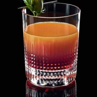 BACCARAT-2811580-Lifestlye-1200w-100KB Baccarat Nancy crystal tumbler filled with a layered cocktail and garnished with a fresh hibiscus bud, showcasing the collection's signature diamond-cut crystal pattern | Kneen & Co