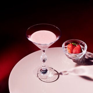 Baccarat Swing crystal bowl filled with fresh strawberries beside a Baccarat crystal cocktail glass on a white tabletop, showcasing the collection's faceted design and brilliant light reflections | Kneen & Co