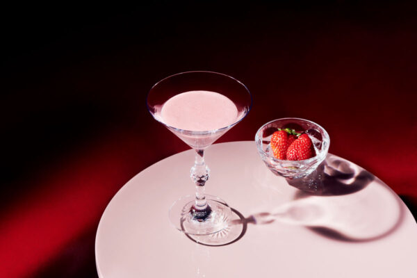 Baccarat Swing crystal bowl filled with fresh strawberries beside a Baccarat crystal cocktail glass on a white tabletop, showcasing the collection's faceted design and brilliant light reflections | Kneen & Co
