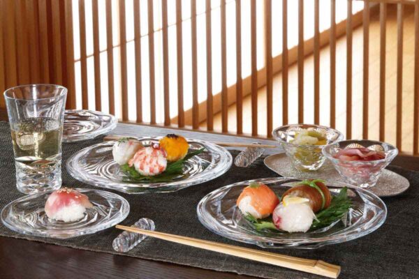 BACCARAT-2814080-Lifestyle-1200w-100KB Baccarat Swing crystal dinnerware and chopstick holders displayed with sushi, crystal bowls, and glassware, showcasing the collection's faceted design and contemporary table setting | Kneen & Co