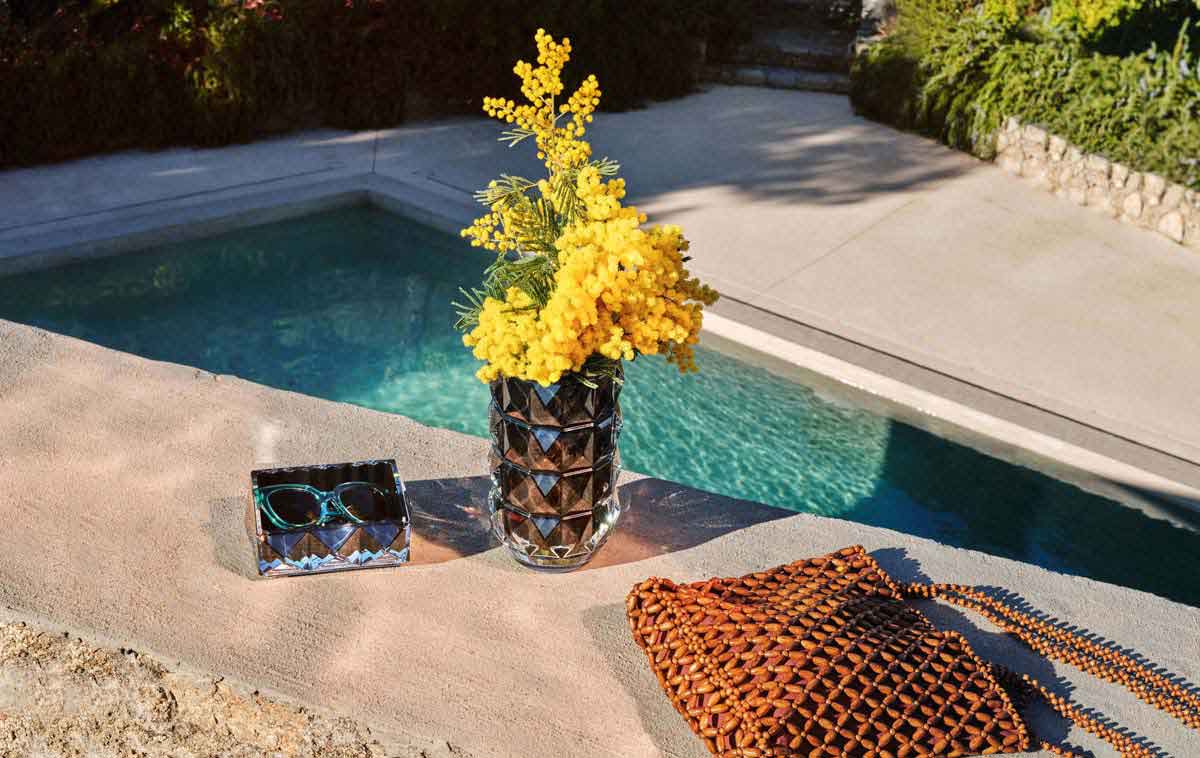 Baccarat Louxor Catch-All Black displayed beside a matching Louxor crystal vase with yellow flowers by a pool, showcasing the collection's geometric faceted design and sculptural elegance | Kneen & Co