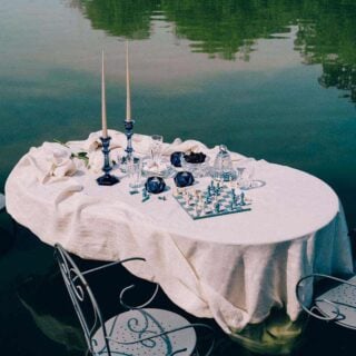 BACCARAT-2818329-2818328-2811288-2815716-Lifestyle-1200w-100KB Baccarat Harcourt 1841 crystal highball glasses displayed on a lakeside table with crystal serveware, blue candlesticks, and a chess set, creating an elegant outdoor setting for cocktails and entertaining | Kneen & Co