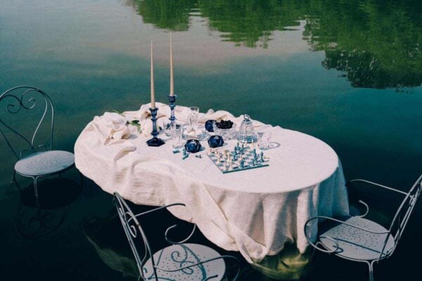 BACCARAT-2818329-2818328-2811288-2815716-Lifestyle-1200w-100KB Baccarat Harcourt 1841 crystal highball glasses displayed on a lakeside table with crystal serveware, blue candlesticks, and a chess set, creating an elegant outdoor setting for cocktails and entertaining | Kneen & Co