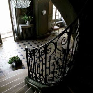 Stone staircase featuring the Lalique Champs-Élysées Chandelier in clear crystal, designed with tiered, frosted oak leaves | Kneen & Co