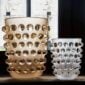 Brightly lit interior setting featuring the Lalique Mossi XXL Vase in clear and frosted crystal with a gold luster finish, side-by-side with a smaller classic clear Mossi vase | Kneen & Co