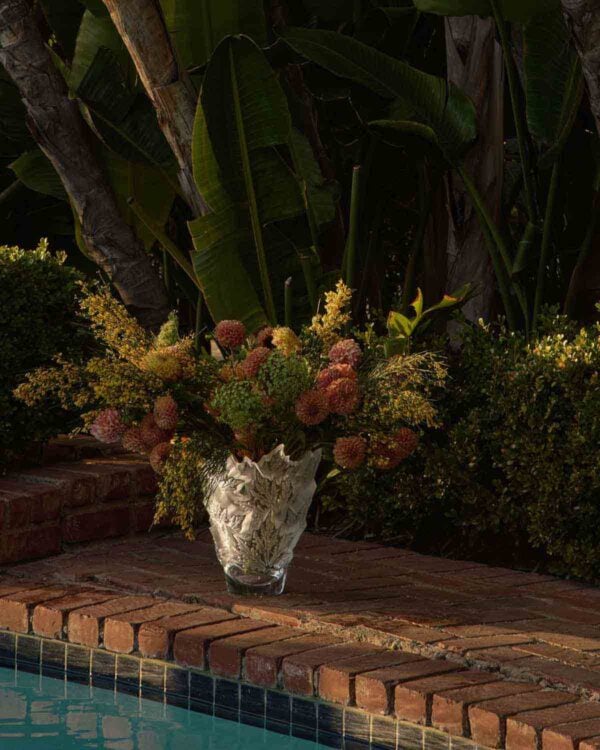 Lush outdoor poolside setting featuring the Lalique Champs-Élysées Vase in clear and frosted crystal | Kneen & Co