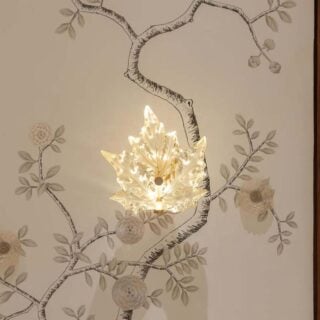 Elegant interior setting featuring the Lalique Champs-Élysées Wall Sconce in clear and frosted crystal, glowing softly to highlight its stylized oak leaf shape | Kneen & Co