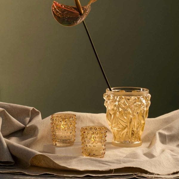 LALIQUE-decorative-crystal-vases-bacchantes-mossi-collection-Nmbr10547600-1200w-100KB Earthy studio setting featuring the Lalique Bacchantes Small Vase in gold-lustre crystal, next to two small glowing votives | Kneen & Co