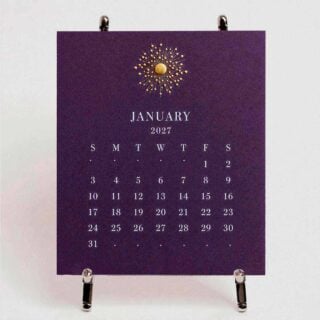 The Printery 2027 Calendar - Aubergine on the chrome easel, white text with starburst engraved in gold | Kneen & Co